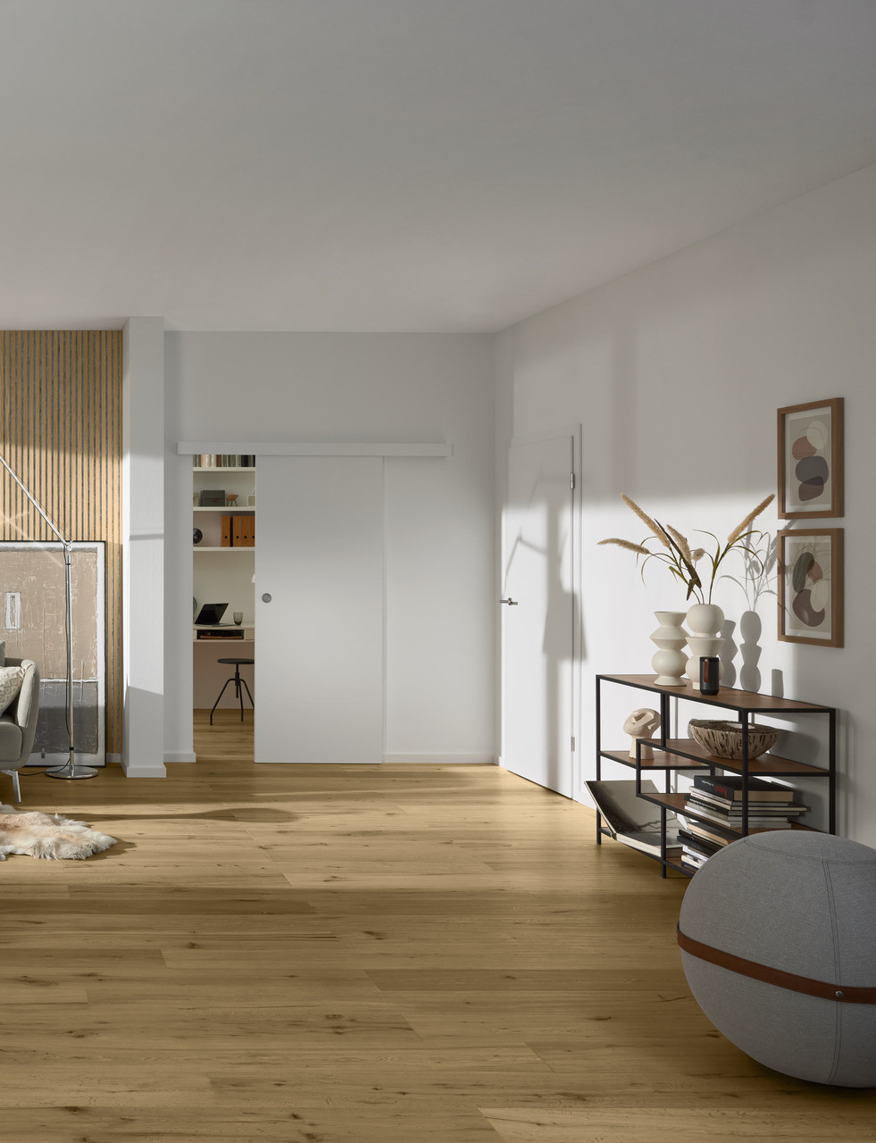 Skandinavisch eingerichtetes Wohnzimmer mit natürlichem Holzboden, Sofa, Sessel, Pflanzen und großer Fensterfront mit viel Tageslicht.