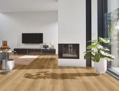 Wohnbereich mit modernem Designboden in warmer Eichenoptik, kombiniert mit Kamin, grauem Sofa und großen Fensterflächen.