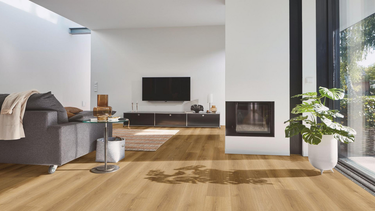 Wohnbereich mit modernem Designboden in warmer Eichenoptik, kombiniert mit Kamin, grauem Sofa und großen Fensterflächen.