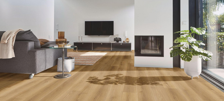 Wohnbereich mit modernem Designboden in warmer Eichenoptik, kombiniert mit Kamin, grauem Sofa und großen Fensterflächen.