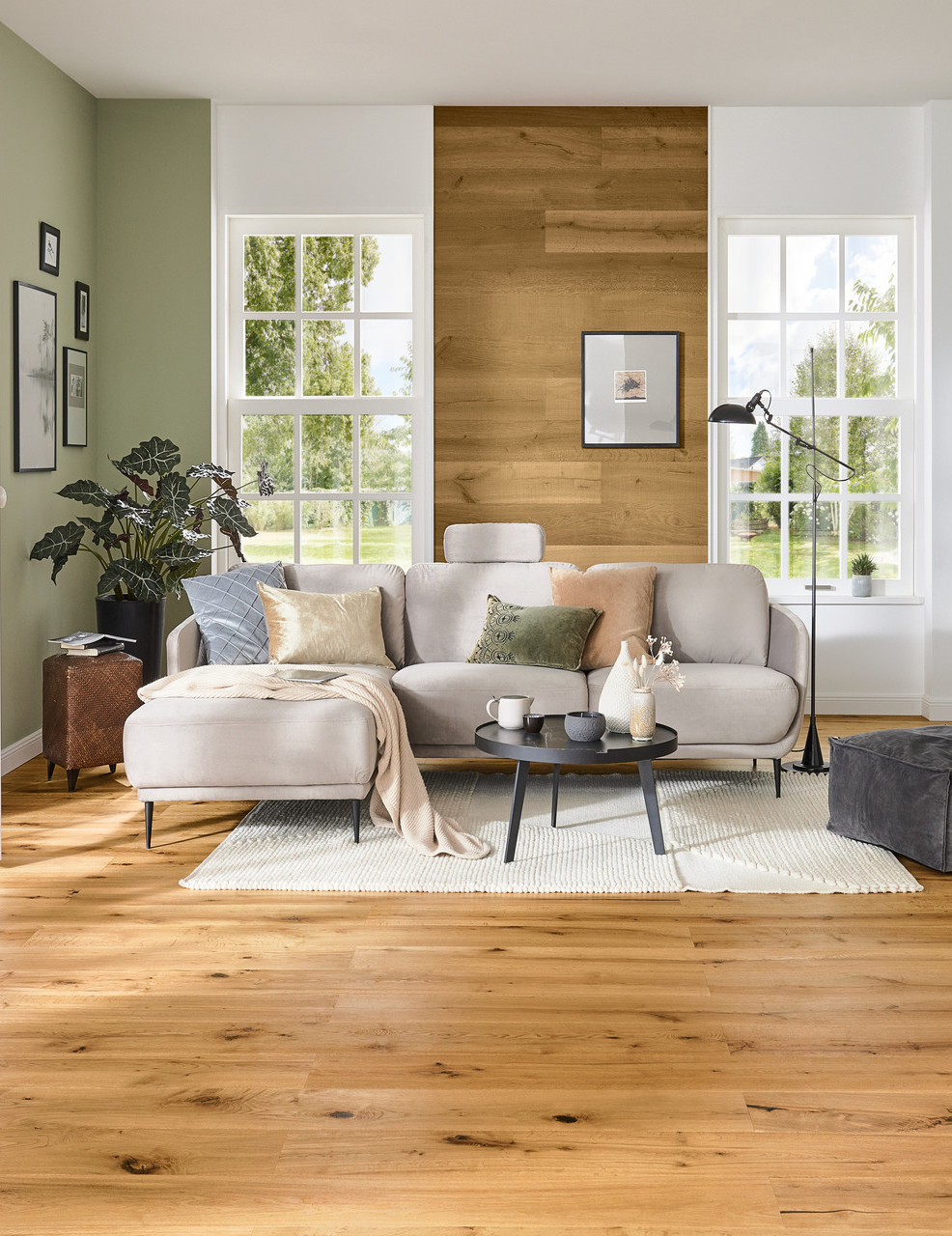 Wohnzimmer im Landhausstil mit hellem Holzboden, Sofa, Couchtisch, Regal und großen Fenstern mit viel Tageslicht.
